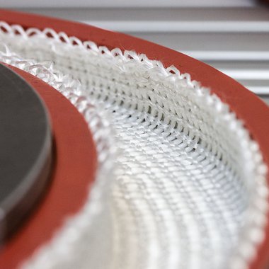 In der Abbildung ist eine Textilstruktur aus Glasfasern zu sehen, die mit einem elastischen Werkzeug umgeformt wird.